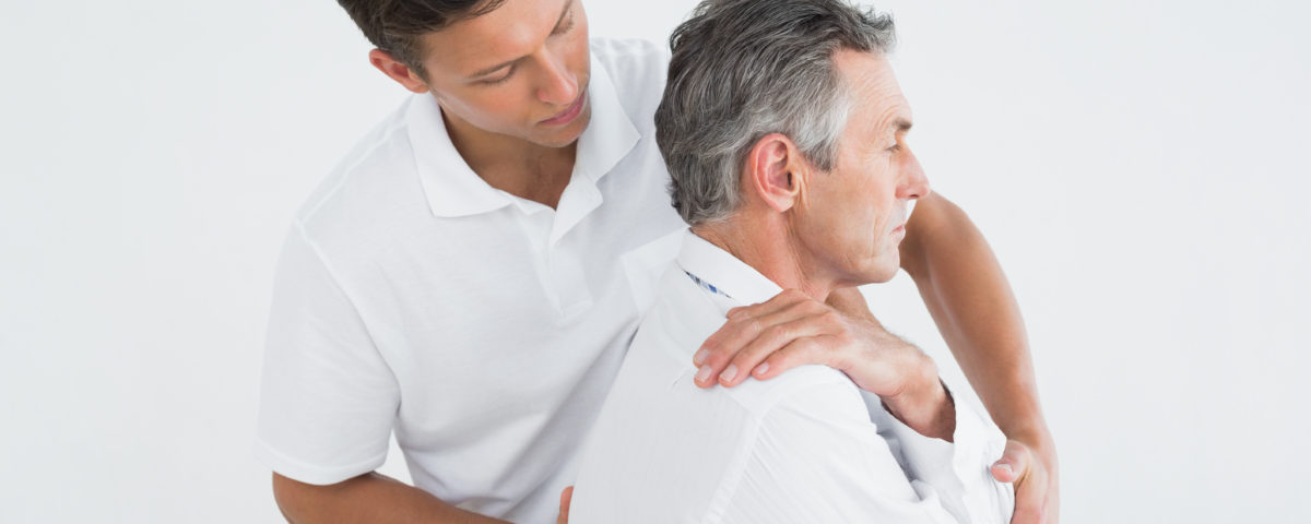 Side view of a male chiropractor examining mature man over white background